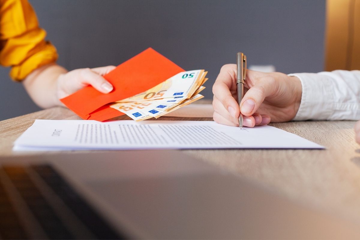 osoba predaje osobi u banci kovertu sa novcem, druga osoba potpisuje dokument